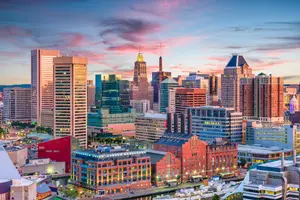 Baltimore skyline with illuminated buildings during sunset, featuring various architectural styles and a waterfront view