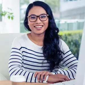 A woman in a striped shirt is sitting at a desk in an office with a cup of coffee in front of her.