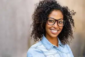Young African American woman with curly hair and glasses smiling at the camera