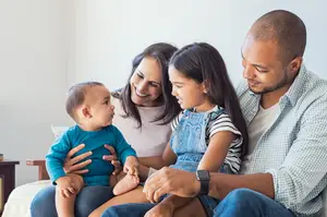 A smiling family of three, a man, a woman, and a young girl sitting on a couch with a baby boy on the woman's lap
