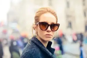 Woman in sunglasses and a blue coat standing on a city street