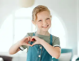 A girl smiling and forming a heart shape with her hands