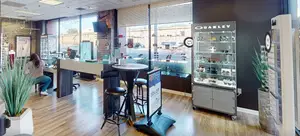 A woman is sitting at a desk in an optical shop, with a sign that reads '30% OFF' and another sign advertising 'SOLD OUT'.