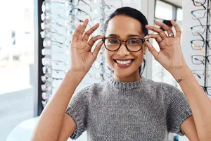 A smiling woman with glasses in front of an optician shop