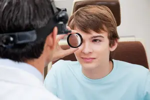 A doctor is examining a young boy's eye with a magnifying glass in a clinic.