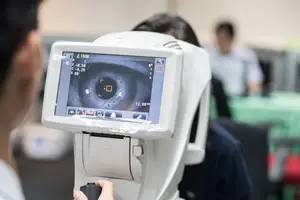 A person is examining an eye with an ophthalmoscope in an indoor setting