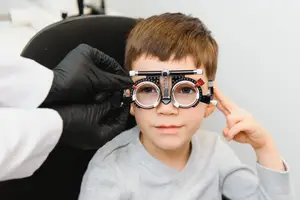 A young boy is wearing a pair of glasses and is looking at the doctor who is adjusting the glasses