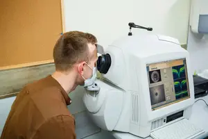 A man wearing a mask and brown shirt looking at a medical machine