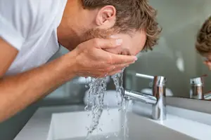 A man washes his face at the sink in a bathroom