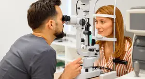 A man is looking through an ophthalmoscope into the eyes of a woman who is smiling at the camera