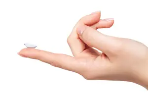 Hand holding a single contact lens on the tip of a finger.