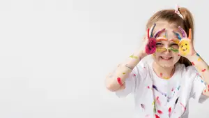 Little girl with paint on her hands and face smiling at the camera