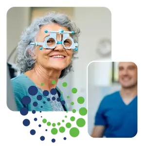 A woman wearing a blue sweater and glasses with a doctor nearby wearing a blue shirt, they are both smiling.