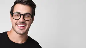 A smiling man wearing glasses and a black shirt against a white background