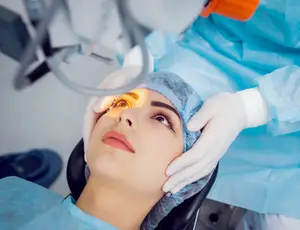 Woman in a blue surgical gown having her eye examined by a doctor wearing blue surgical attire and gloves