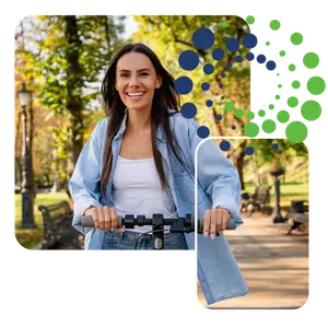 A woman is riding a scooter in a park with trees and benches in the background.