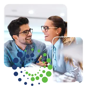 A man and a woman in glasses are smiling at each other, likely colleagues or business partners in a professional setting.