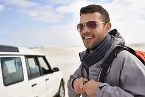 Man smiling and adjusting his jacket while wearing sunglasses and a scarf