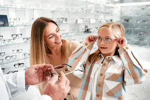 A woman and a child are trying on glasses in a store with a man behind them