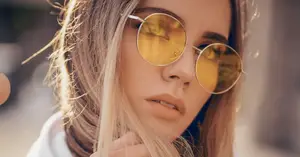 Close up of a woman with blonde hair and gold sunglasses looking at the camera