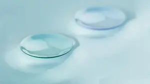 Close up of two water droplets on a white surface with a slightly blurry background.