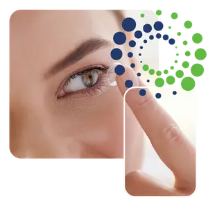 A person is inserting a contact lens into their eye while another person's finger is holding the lens.