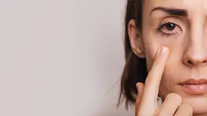 A woman applying skincare product near her eyes with her finger