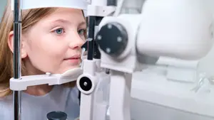 A girl with blonde hair is looking through an eye exam machine