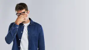 A man with glasses covering his face with his hand looking to the side