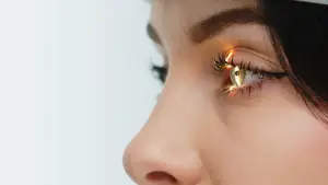 Woman with black hair and light brown eyes with a yellow light reflection in the iris