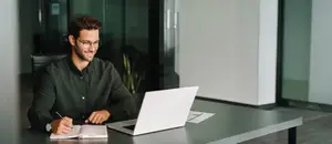A man sitting at a desk and writing on a notebook with a pen.
