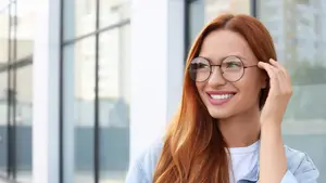 Redhead woman in white t-shirt and denim jacket with round glasses smiling