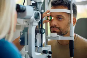 A man is examining his eyes using an ophthalmoscope while a woman observes.