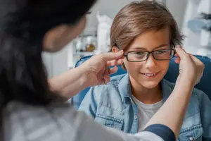 A woman is adjusting a child's eyeglasses in a doctor's office.