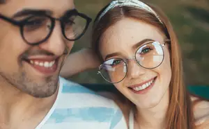 A couple smiling at the camera, the man in glasses and the woman in sunglasses