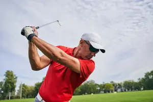 A golfer swings their club outdoors on a golf course