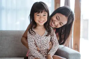 A girl and a woman are sitting on a couch and smiling at the camera