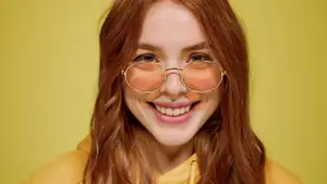 Woman with red hair wearing a yellow hoodie and sunglasses smiling for a photo