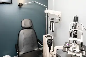 A room with a black leather chair and a white and black ophthalmoscope on a table.