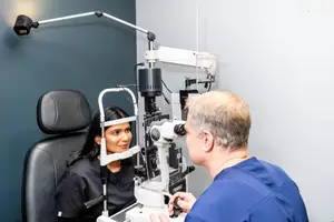 An eye doctor examines a patient's eye with a slit lamp in a medical office.