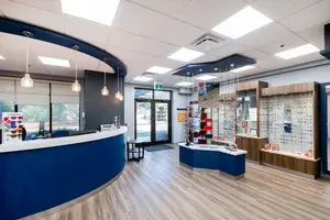 A modern and inviting interior of an optometrist's office with a reception desk, glass doors, and an array of eyewear on display.
