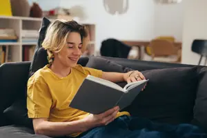 A person reading a book on a couch while smiling