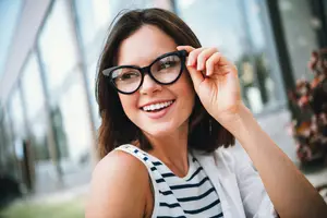 A woman adjusting her glasses and smiling