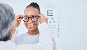 A smiling woman is adjusting her glasses with the help of an older man wearing a white long-sleeved shirt