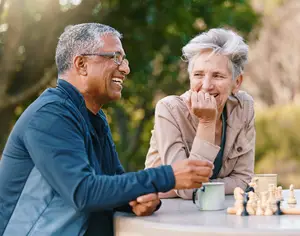 A smiling elderly couple playing chess in a park