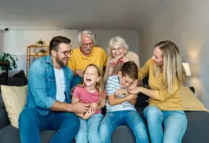 A family is sitting on a couch and appears to be laughing while looking at something on the right side
