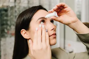 Woman applying eye drops in front of a mirror