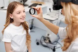A young girl is having her eyes checked by a female doctor in a white lab coat