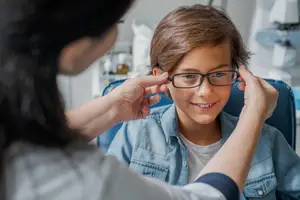A woman is adjusting a boy's glasses in a clinic.