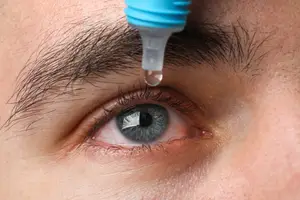 Close up of someone using eye drops in their right eye.
